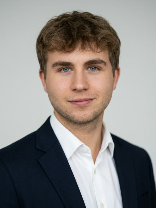 Julian Berger, Porträtfoto: dunkles Sakko, weißes Hemd, heller Hintergrund